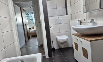 A modern bathroom with a bathtub and a sink on a wooden vanity. The walls are brightly tiled, and there is a view of an adjacent room.