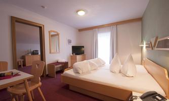 A cozy hotel room with a double bed and a seating area. There is a table, a television, and plenty of daylight through a window.