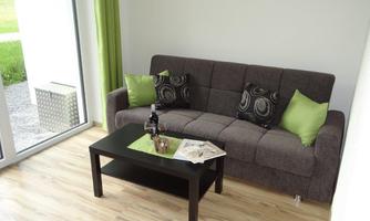 A modern living room with a gray couch and green cushions. On the table are wine and magazines.