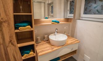 A modern bathroom with a sink and wooden shelves. Towels in various colors are neatly arranged.