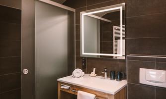 A modern bathroom with an elegant shower and a simple sink. The large mirror and dark tiles give the space a stylish atmosphere.