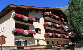 A charming building with balconies decorated with colorful flowers. In the background, there are trees and a clear blue sky.