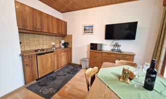 A cozy kitchen with wooden cabinets and modern appliances. A dining table with a bottle of wine and a glass is ready.