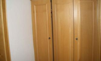 A wooden cupboard with three doors. The doors are closed and the wood surface is smooth and light.