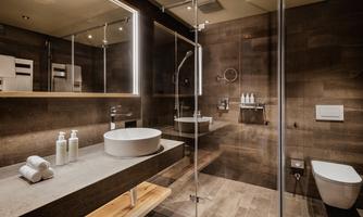A modern bathroom with a large shower and stylish sink. The walls are in warm tones, and there are toiletries placed on the shelf.