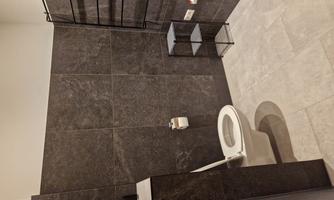 A modern bathroom with dark tiles. A toilet and an open shelf are visible.