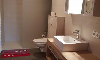 A modern bathroom with a wooden ceiling. It includes a sink, a toilet, and a floor covering of gray tiles.