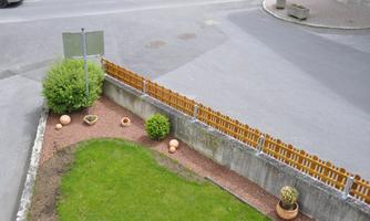 A well-maintained garden with a lawn, small plants, and flower pots. In the background, a slope and a wooden fence can be seen.