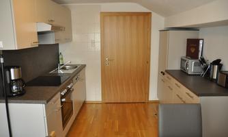 A modern kitchen with bright furniture and wooden flooring. It includes essential appliances such as a stove, a microwave, and a coffee machine.