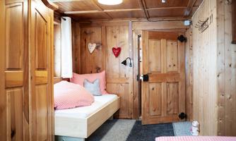 A cozy room with wood-paneled walls and a bed with checkered pillows. An open door reveals access to another area.