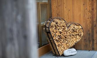 A heart made of wooden logs stands against a wooden wall. There is also a small stone with the inscription "Welcome."