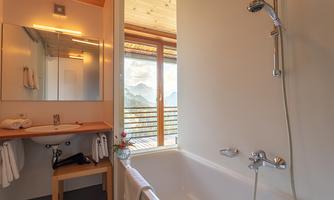 A modern bathroom with a bathtub and a large window that offers a view of the mountains. The warm wood elements create an inviting atmosphere.