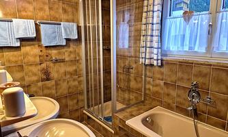 A bathroom with brown tiles and a shower. There are two sinks, a bathtub, and windows with curtains.
