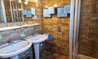 A modern bathroom with two sinks and a shower. The walls are tiled in brown, and there are several towels in shades of blue.