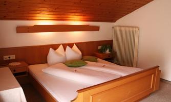 A cozy bedroom with wooden paneling and a double bed. The pillows are arranged symmetrically and the walls are light-colored.