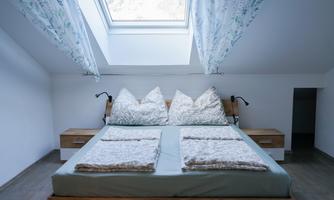 A modern bedroom with a large bed and natural wooden furniture. Bright curtains and a skylight provide plenty of daylight.