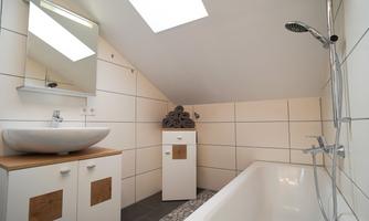 A modern bathroom with a bathtub, a sink, and a large mirror. The walls are brightly tiled and light flows through a skylight.