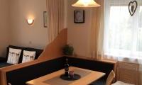 A cozy dining area with a wooden table and chairs. The windows let in plenty of light, and there is a decorative lamp.