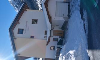 A modern holiday home in the mountains, surrounded by snow. The sky is clear and the view of the mountains is impressive.