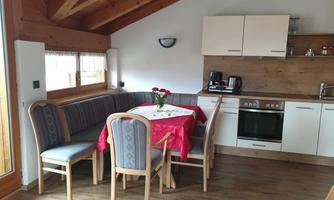 A cozy kitchen with wooden paneling and a dining area. The table is decorated with a red tablecloth and a flower vase.