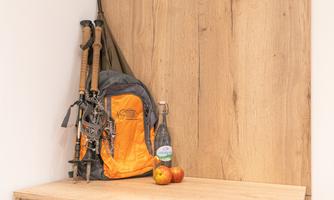 A backpack with hiking poles is on a wooden table. Next to it are two apples and a bottle of water.