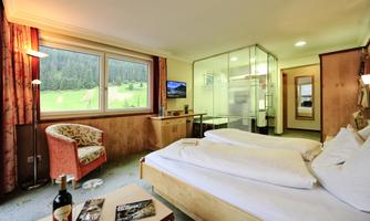 A cozy hotel room with two beds, a television, and large windows overlooking nature. The decor is modern and welcoming, featuring a small table and an armchair.