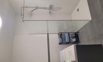 A modern bathroom with a glass shower and a freestanding bathtub. In the corner, there is a shelving system with towels.