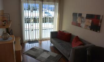 A bright living room with a gray sofa and colorful cushions. Large windows let in plenty of light and offer a view outside.