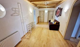 A bright hallway with wooden flooring and a cozy sofa. Mirrors and a piece of art hang on the wall, while a coat rack is set up.