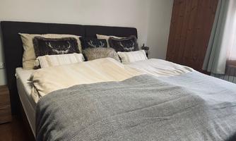 A cozy bedroom with a large bed adorned with cushions and soft blankets. The walls are bright, and there are wooden details that convey a warm impression.