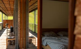 A modern room with a bed and wooden paneling. The view leads to a terrace surrounded by nature.