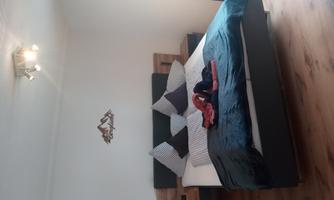 A modern bedroom with a large bed and several pillows. A cozy atmosphere with wooden flooring and soft lighting.