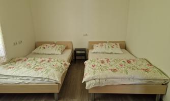 A room with two separate beds and simple furniture. The bedding is decorated with floral patterns.