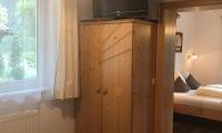 A cozy room with a wooden wardrobe and a television. In the background, a bedroom with a bed is visible.