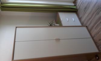 A bright room with a white wardrobe and a dresser. On the sideboard, there is a small plant, and large windows let in a lot of light.