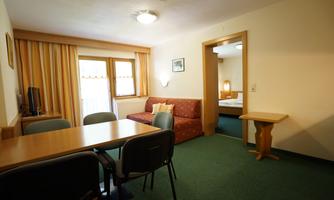 A cozy living space with a dining table and chairs. In the background, there is a sofa and access to a bedroom.