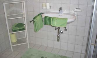 A modern bathroom with a sink and towels in green tones. There is a towel rack and a shower in the background.