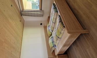 A cozy bedroom with a double bed and wooden decor. The room has a window with curtains and a wooden floor.