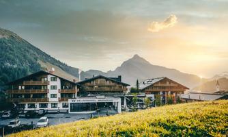 A picturesque hotel in the mountains at sunset. The surroundings are green and offer a stunning view of the mountains.