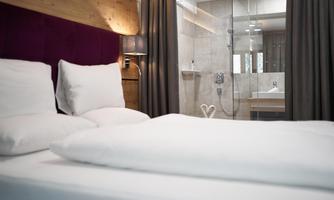 A modern bedroom with a comfortable bed and soft pillows. In the background, there is an elegant bathroom with a glass shower.