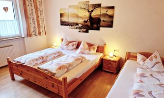 A cozy room with three wooden beds. A decorative picture of a deer in a landscape hangs on the wall.
