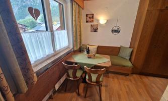 A cozy dining area with wood paneling and a round table. The windows offer a view of a beautiful mountain landscape.