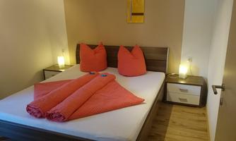 A cozy bedroom with a double bed and red pillows. Next to the bed, there are two nightstands with lamps.