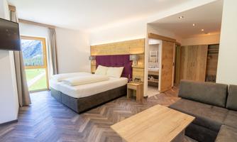 A modern hotel room with a large bed and a cozy sofa. Large windows offer views of nature.