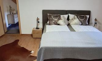 A cozy bedroom with a large bed and decorative cushions. The floor is furnished with a rug made of animal hide.