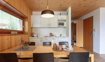 A modern kitchenette with a wooden dining area. There is a table with chairs, decorated with flowers and dishes.