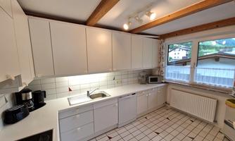 A bright and modern kitchen with white cabinets and a large window front. The room is well-equipped and has a cozy atmosphere.