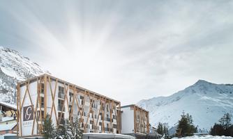 A modern hotel amidst snowy mountains. The sun shines behind the mountains.