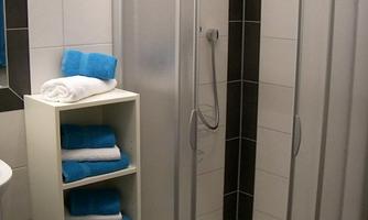 A modern shower with transparent glass doors stands in a bathroom. Next to the shower is a shelf with blue towels.