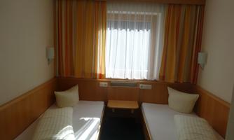 A simple room with two single beds and bright, striped curtains. A window provides plenty of natural light.